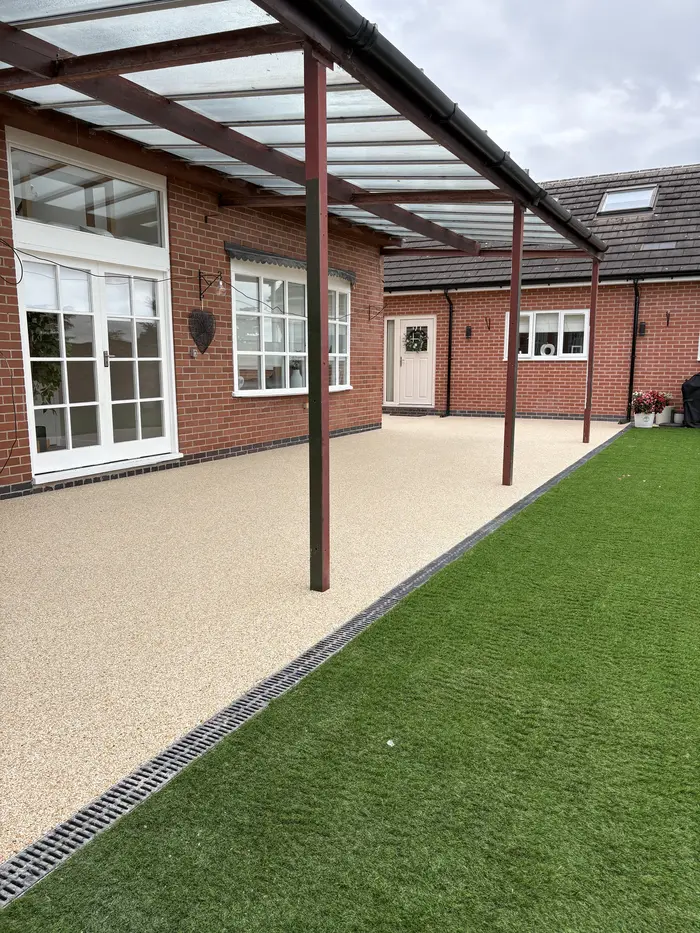 Cream resin bound patio under a pergola beside artificial grass, by A&P Resin