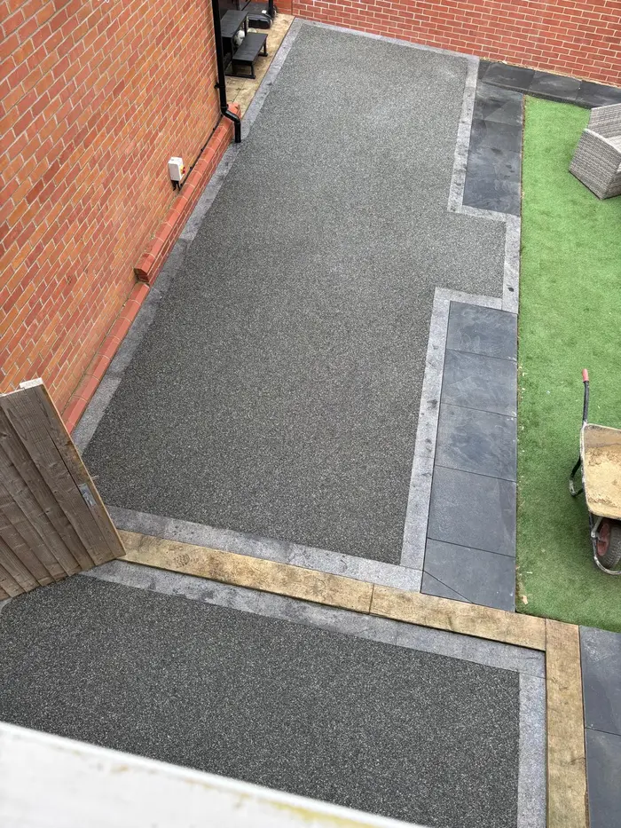 Grey resin bound patio with charcoal border and artificial grass, by A&P Resin