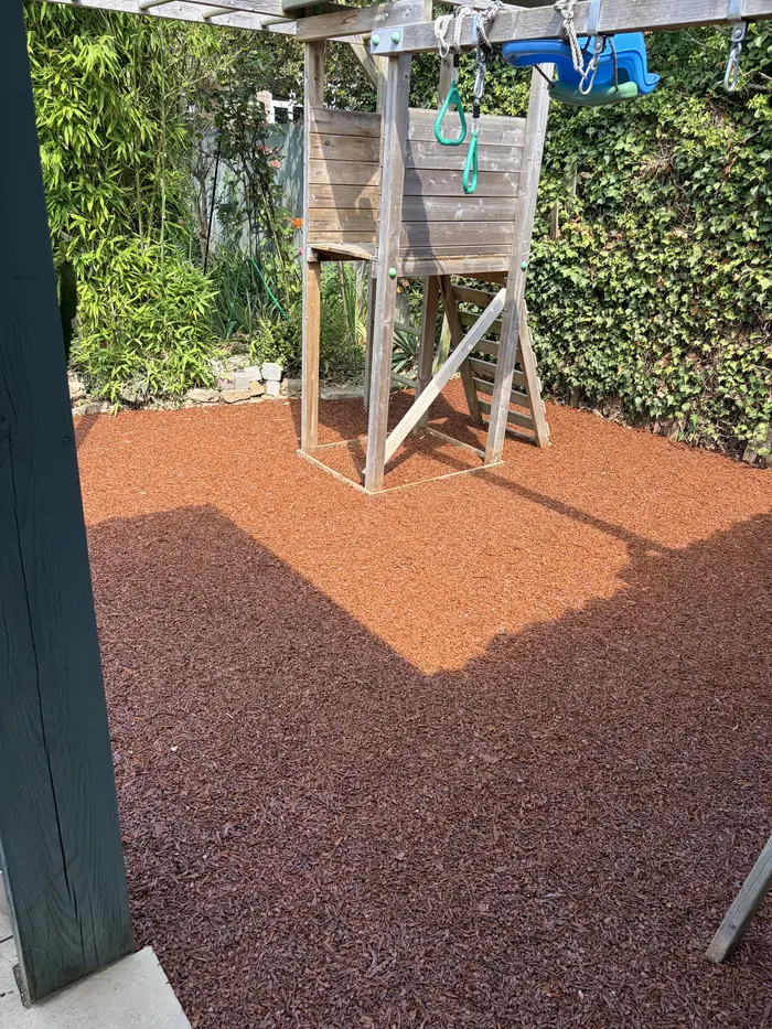 Red rubber mulch play area with a wooden climbing frame, by A&P Resin